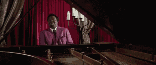 a man in a purple suit and tie is playing a piano