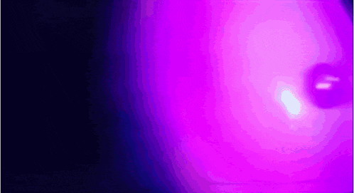 a purple light is shining on a black background in a dark room .
