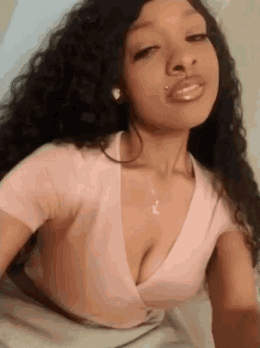 a woman with curly hair is wearing a pink crop top and a necklace .