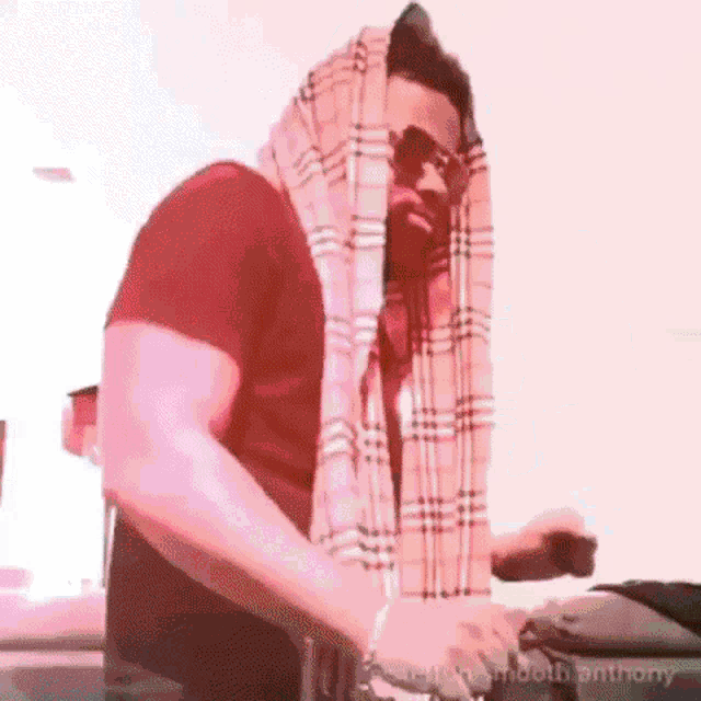 a man wearing a red shirt and a plaid scarf around his head is sitting at a table .