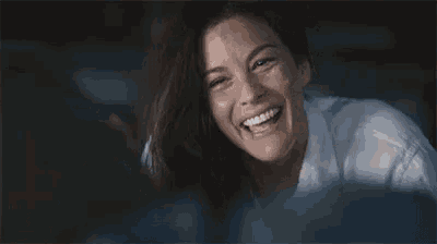 a woman is smiling and looking at the camera while sitting in a dark room .
