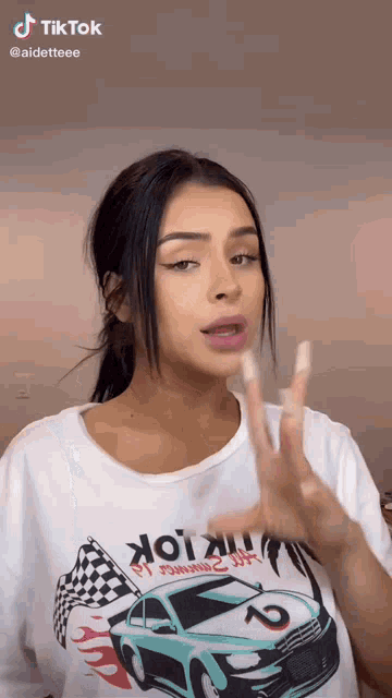 a woman wearing a white t-shirt with a race car on it is making a hand gesture .