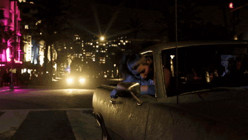 a woman is sitting in a car with her head out the window at night