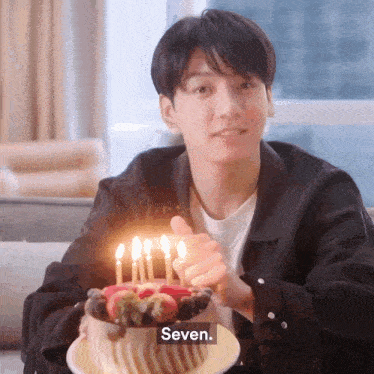 a young man is holding a cake with candles and giving a thumbs up sign