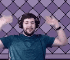 a man wearing headphones and a blue shirt is dancing in front of a purple checkered wall .