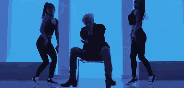 a man sitting in a chair is surrounded by two women who are dancing