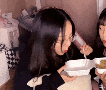a girl wearing glasses is holding a styrofoam container with a spoon in it