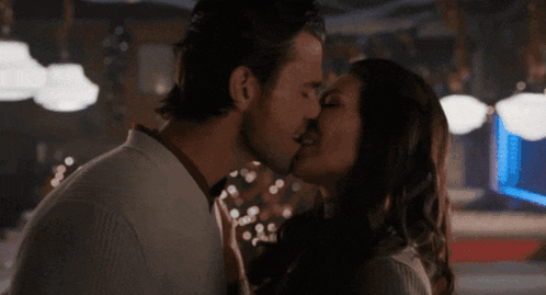 a man and woman are kissing in a dark room with christmas lights in the background