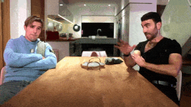two men are sitting at a table with their arms crossed and one is talking