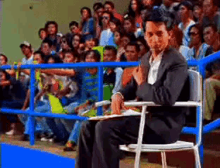 a man in a suit is sitting in a chair in front of a crowd of people