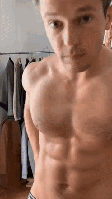 a shirtless man is standing in a room with clothes hanging on a rack .