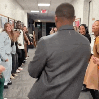 a man in a suit is standing in a hallway with a group of people standing around him .