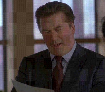 a man in a suit and tie is reading a piece of paper with his mouth open .