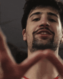 a man with a beard is smiling and making a heart with his hands