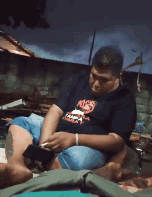 a man wearing a t-shirt that says tanpa harat looks at his phone