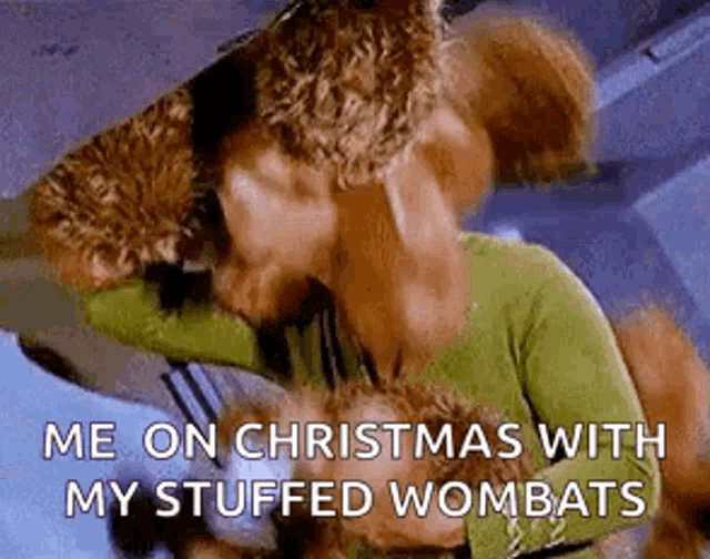 a stuffed wombat is laying on a bed with a christmas tree in the background .