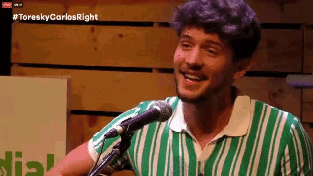 a man in a green and white striped shirt is singing into a microphone with #toreskycarlosright written on the bottom