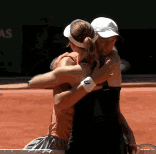 two female tennis players hugging on a court with asics on their wrists