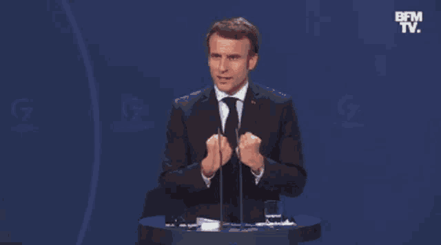 a man in a suit and tie is giving a speech at a podium with bfm tv behind him