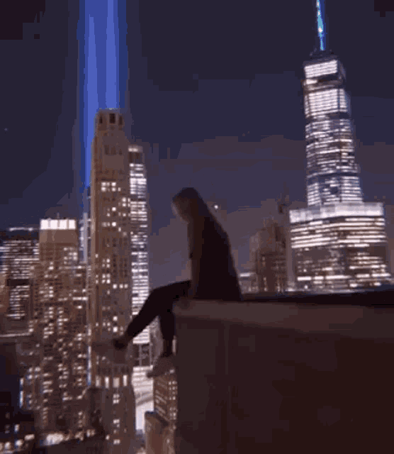 a woman is sitting on the edge of a building in front of a city skyline .