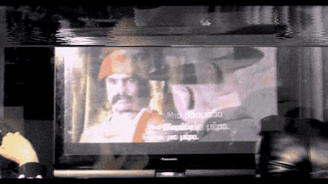 a tv screen shows a man with a beard and a red hat with a foreign language on it