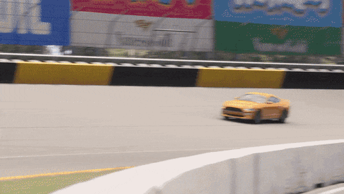 a yellow car is driving on a race track with a sign in the background that says alberta