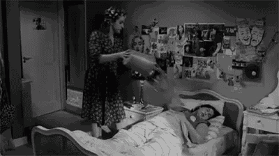a black and white photo of a woman standing next to a girl laying in a bed .