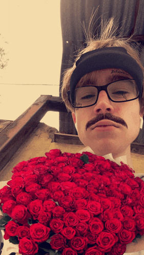 a man with glasses and a mustache holds a bunch of red roses