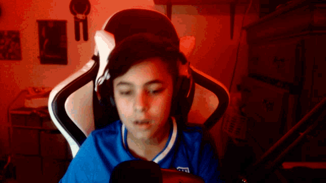 a boy wearing headphones and a blue shirt that says ' a ' on it sits in front of a microphone