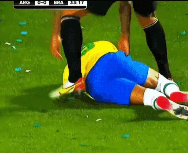 a soccer player is laying on the ground while another player kicks his butt .