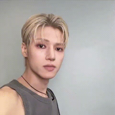 a young man with blonde hair is making a funny face while wearing a grey tank top .