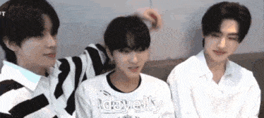 three young men are sitting next to each other on a couch and one of them is touching the other 's hair .