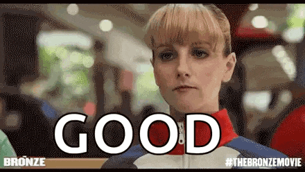 a woman is standing in front of a sign that says `` good '' and is looking at the camera .