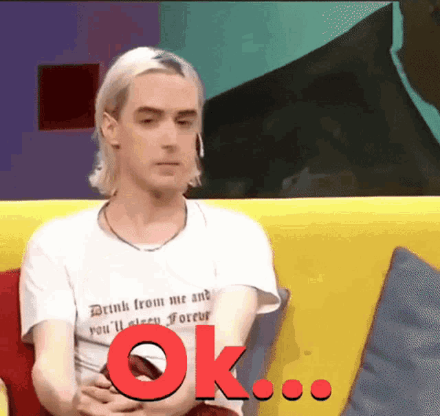 a man wearing a white shirt that says drink from me and you 'll sleep forever sitting on a yellow couch