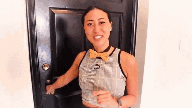 a woman wearing a bow tie and a crop top is opening a door .