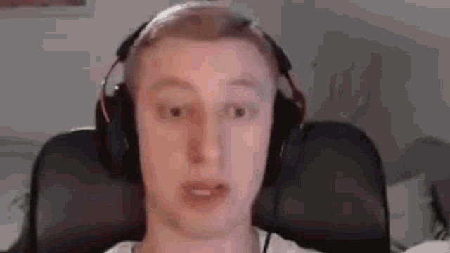 a young man wearing headphones is sitting in a chair and making a funny face .
