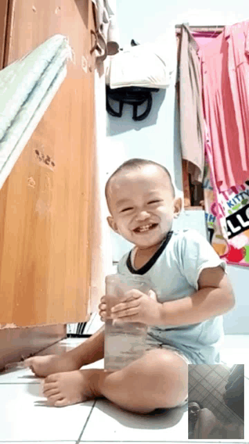 a little boy is sitting on the floor holding a glass and smiling