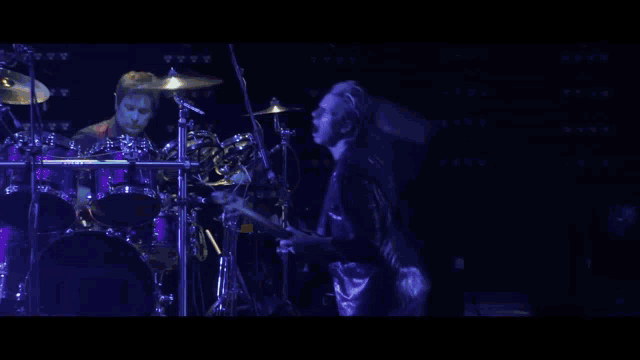 a man playing a guitar on a stage with a drummer behind him