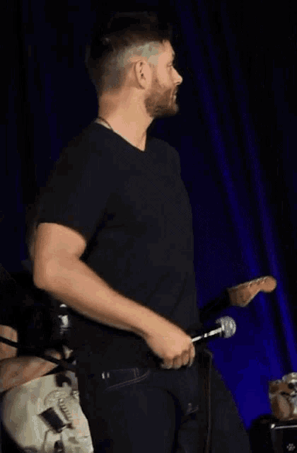 a man in a black shirt is holding a guitar and a microphone .
