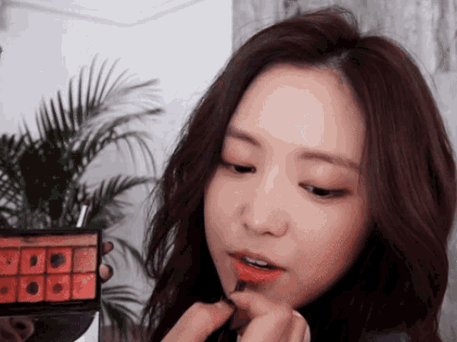 a woman is applying red lipstick while holding a palette