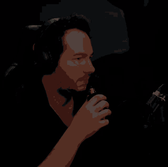 a man wearing headphones sits in front of a microphone with his hand on his mouth