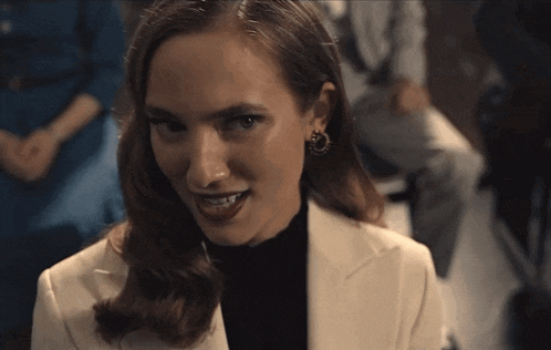 a woman wearing a white jacket and black turtleneck looks at the camera