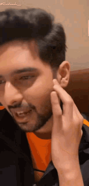 a man with a beard is touching his ear with his hand and smiling .