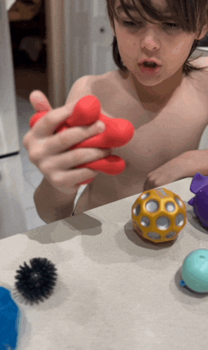 a shirtless boy is holding a red ball in his hands