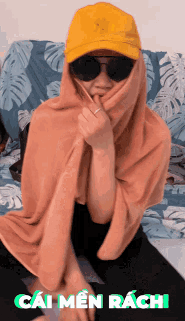 a woman wearing a yellow hat and sunglasses is wrapped in a blanket and says cai men rachi