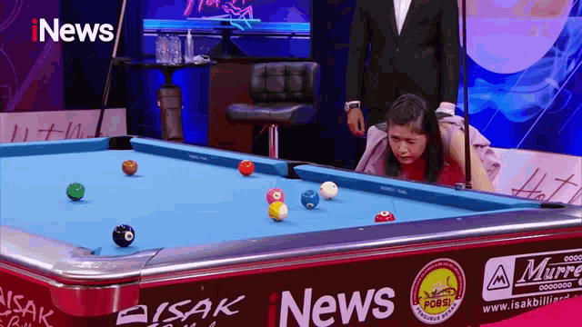a woman is playing pool in front of a pool table sponsored by i news