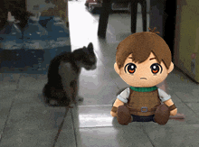 a stuffed boy is sitting on the floor while a cat looks on