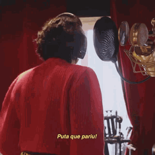 a woman in a red sweater stands in front of a microphone with eu quase urinel in yellow letters