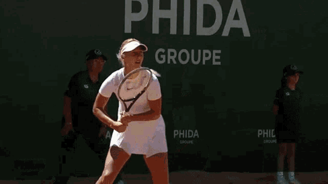 a woman is holding a tennis racquet in front of a green sign that says hida groupe