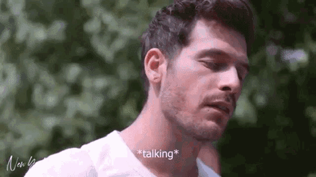 a man with a beard is wearing a white shirt and talking to someone .